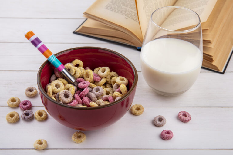 top view of colorful cereals on a red bowl with spoon with a glass of milk on white background